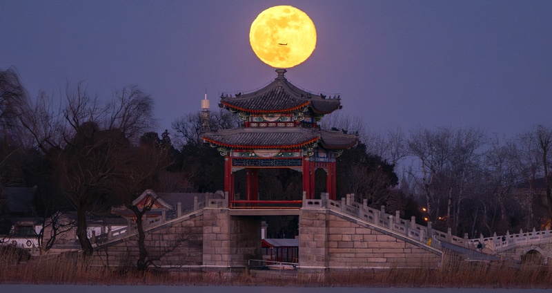 A plane fly by round moon on the top of the Lian Bridge Pavilion