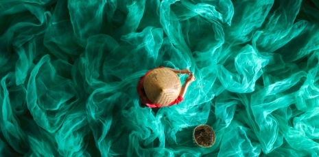 Worker mending fishing nets immersed in emerald-green "ocean"